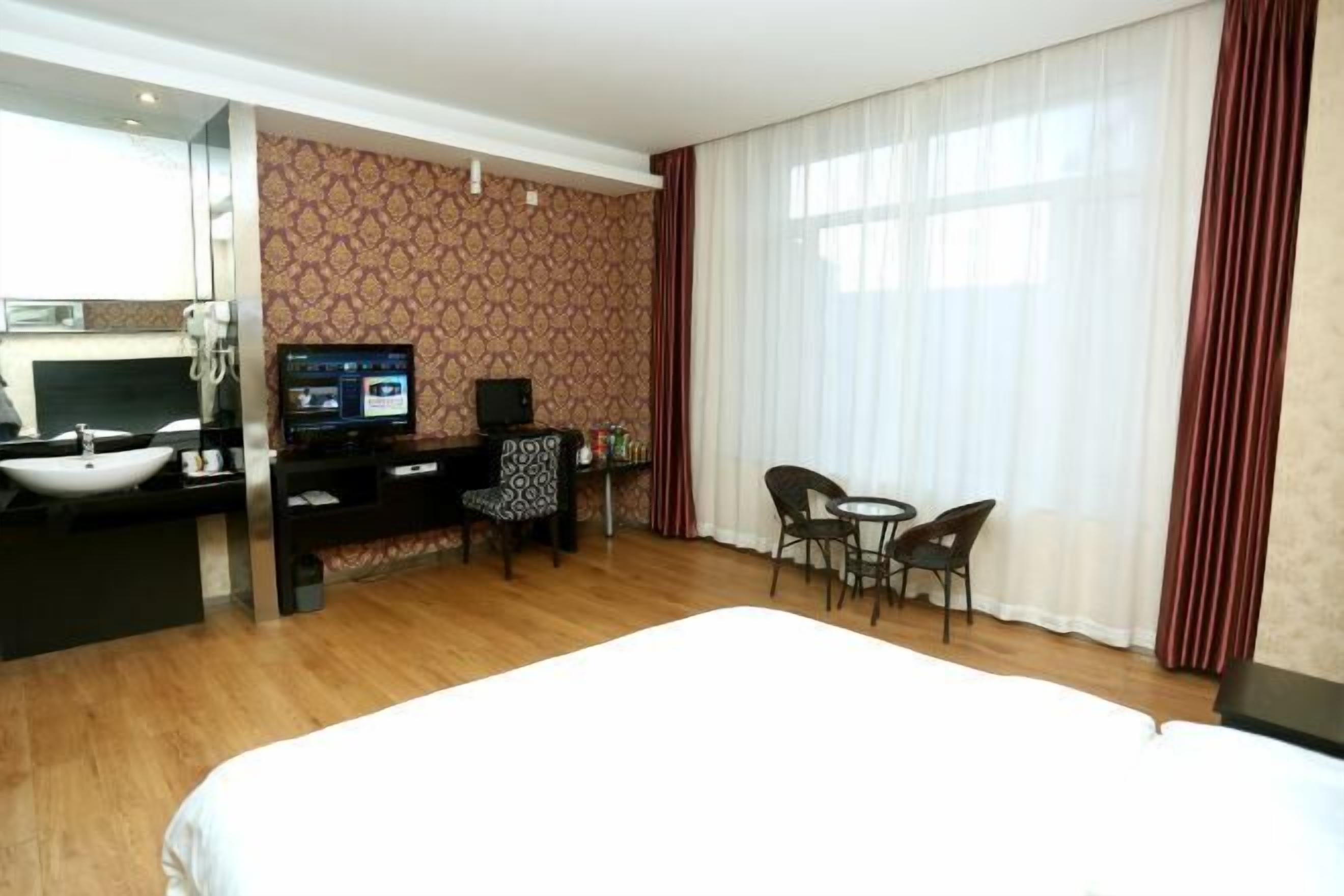Quarto de hotel com cama, escrivaninha com computador, televisão, cadeira e uma mesinha.
