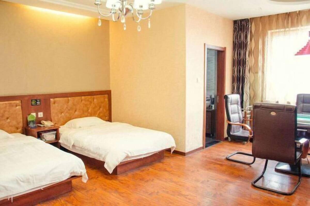 Ett hotellrum med två sängar, ett skrivbord, en stol, en kristallkrona och ett fönster med gardiner.