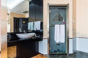 Un baño moderno con tocador negro, lavamanos blanco y cabina de ducha con mampara de vidrio.