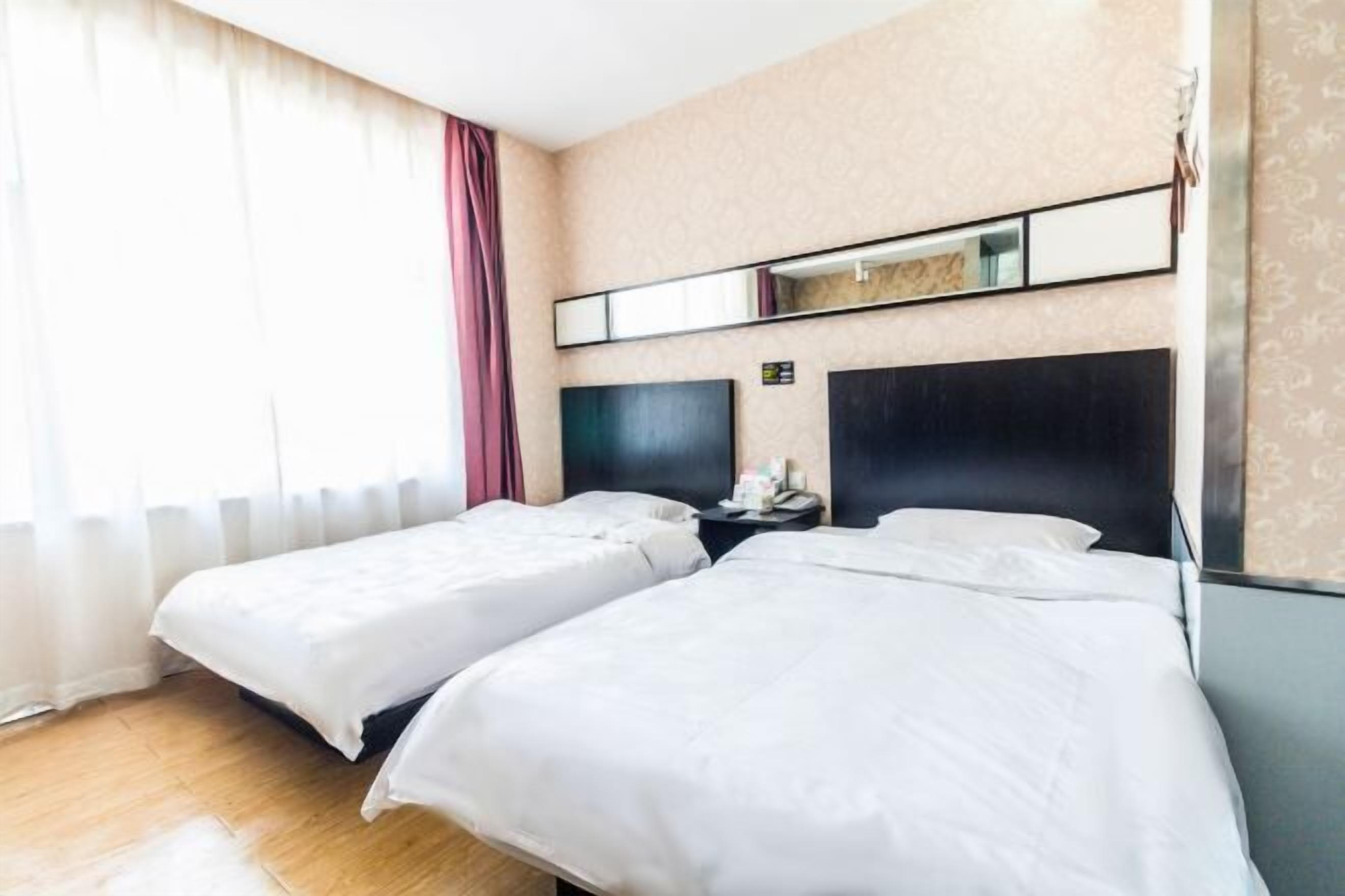 Een hotelkamer met twee bedden, een grote spiegel boven het hoofdeinde en een nachtkastje met een telefoon en een lamp.