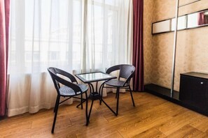 Ein Zimmer mit Holzboden, einem Glastisch, zwei Korbstühlen, einem schwarzen Schrank und einem Spiegel an der Wand.