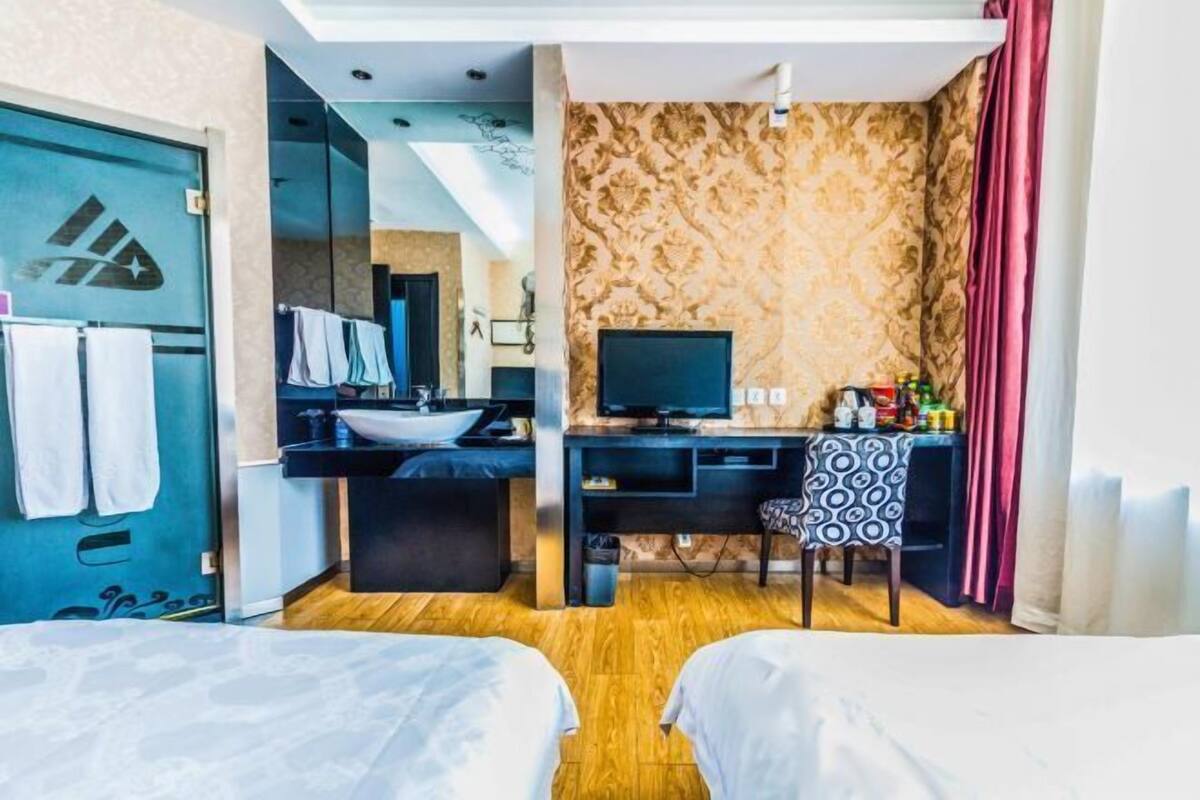 Ett hotellrum med två sängar, ett skrivbord med en dator, ett handfat och en spegel.