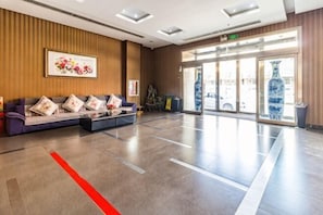 Eine Hotelhalle mit einer Rezeption, einer Couch mit Kissen, einem gerahmten Kunstwerk und einer großen Vase.