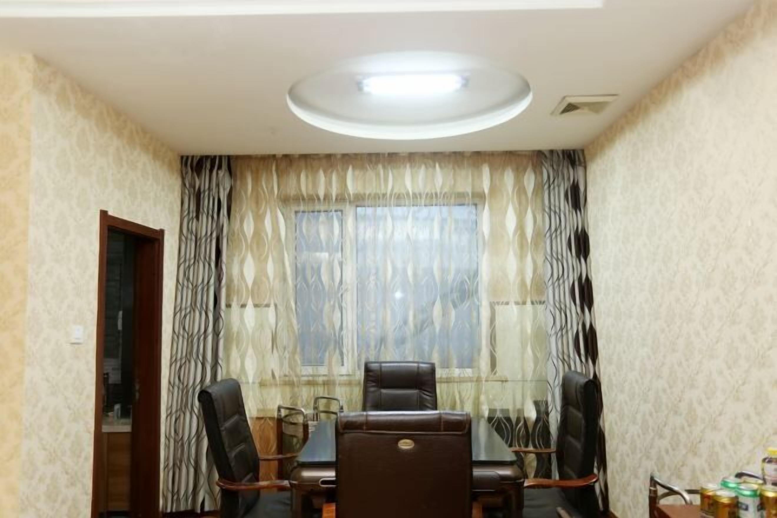 A conference room with a table and chairs, a window with patterned curtains, and a ceiling light.