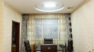 A conference room with a table and chairs, a window with patterned curtains, and a ceiling light.