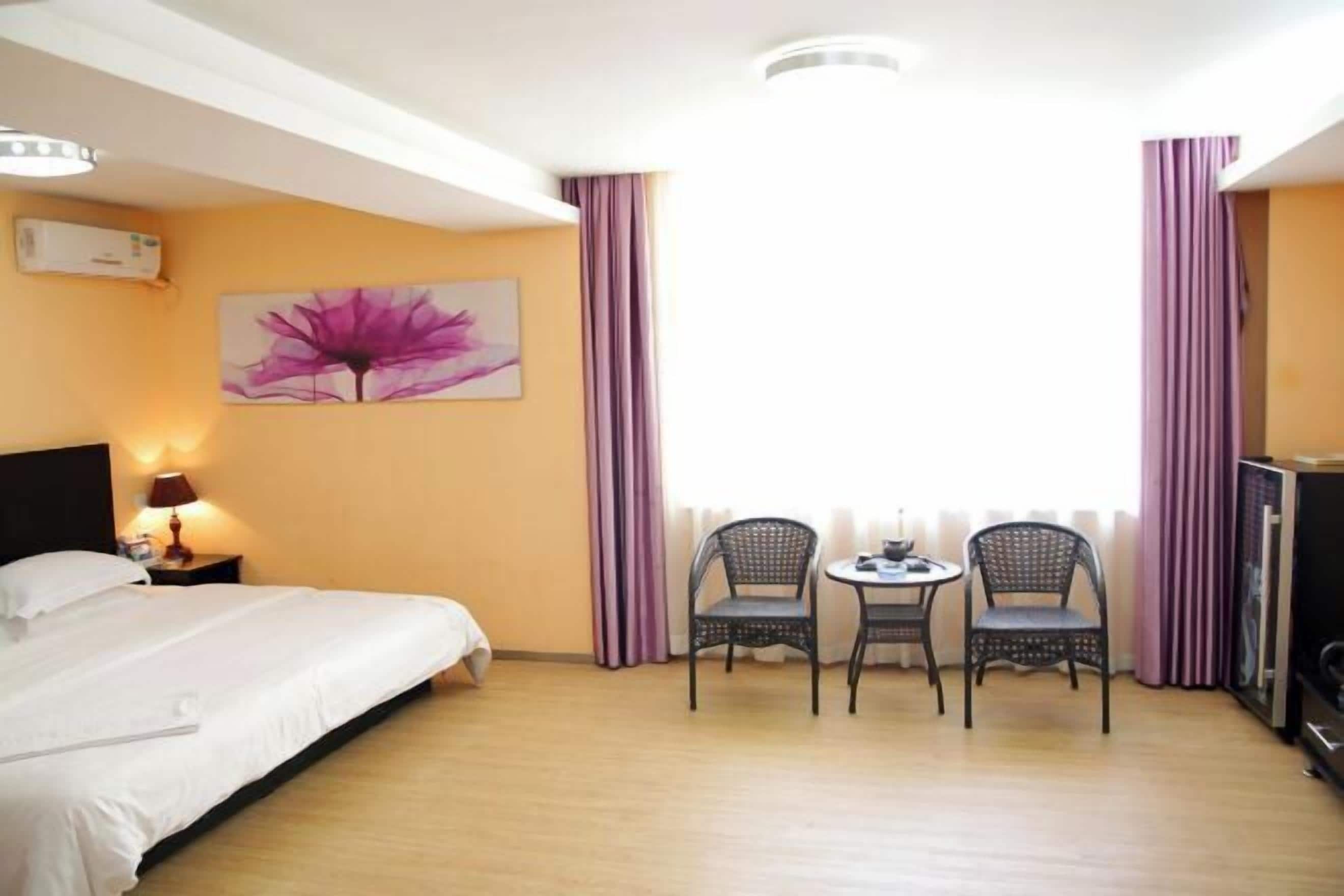 A hotel room with a bed, two chairs, a small table, a TV, and a window with curtains.