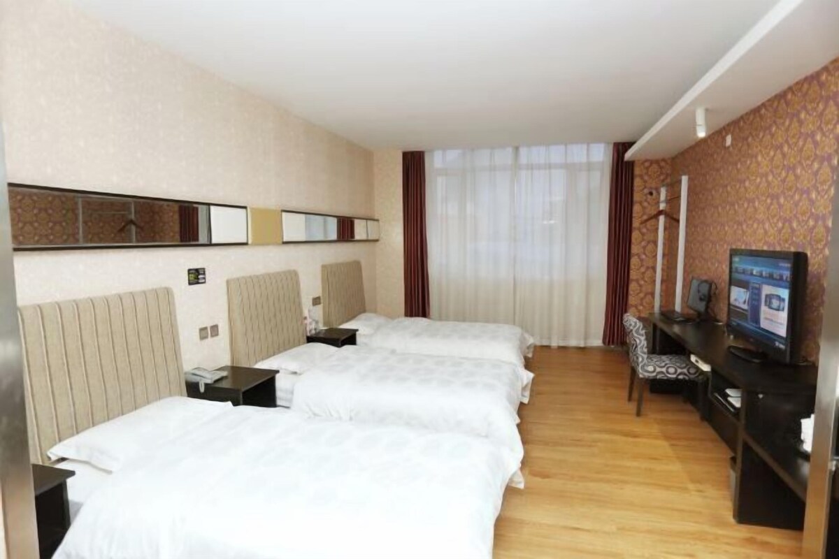 A hotel room with three beds, a TV, a desk, and a chair.