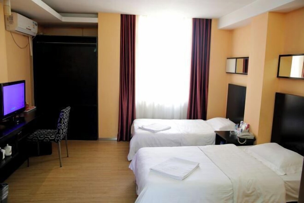 A hotel room with two beds, a desk with a computer, a chair, and a TV.