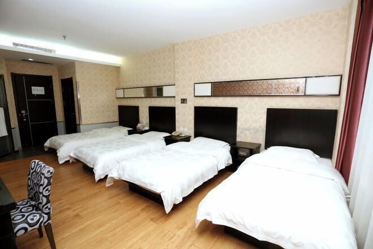 A hotel room with three single beds, a desk, and a chair.
