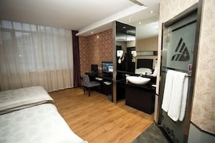 Habitación de hotel con cama, escritorio con computadora, baño con lavamanos y espejo, y un amplio ventanal con cortinas.