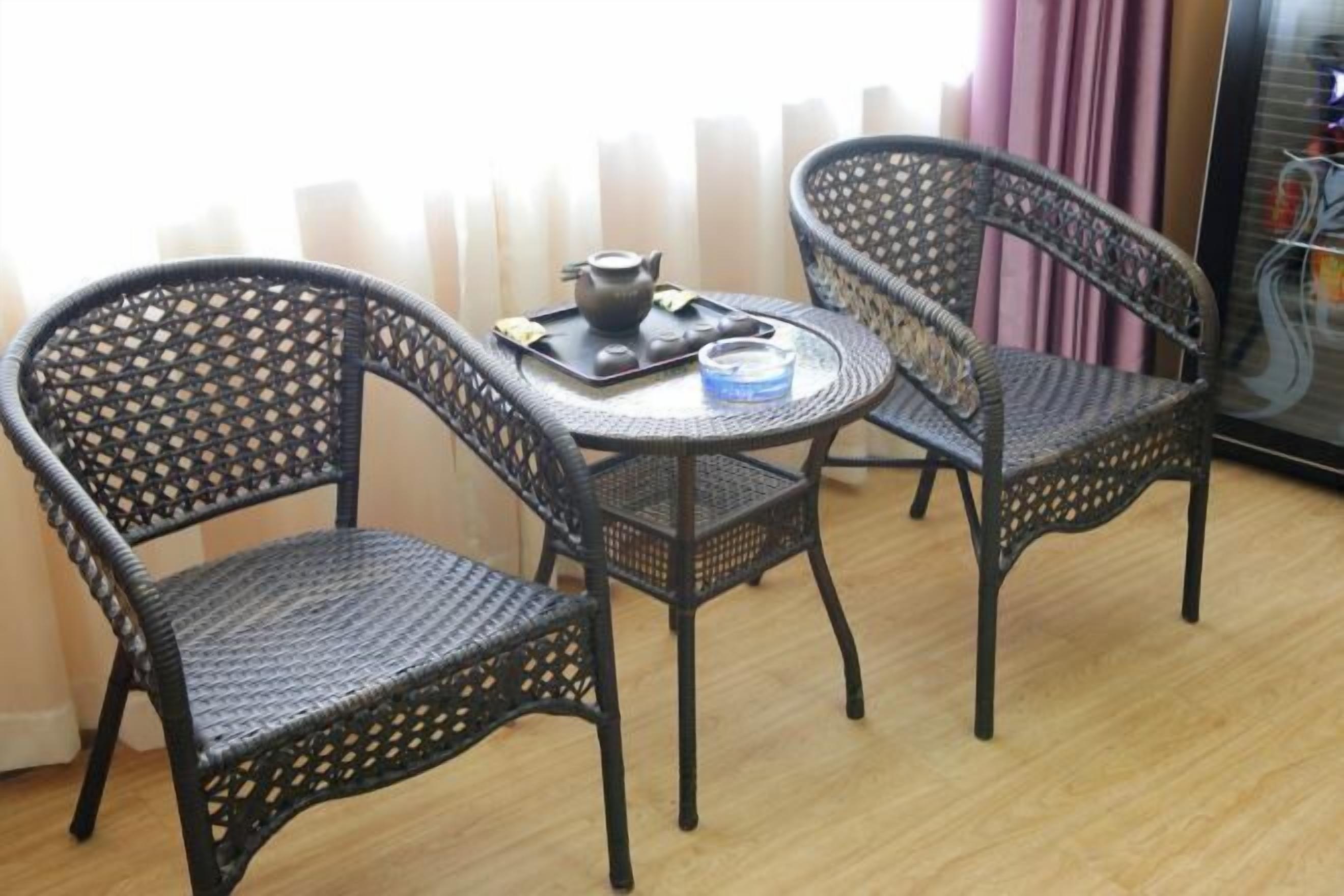 A room with two wicker chairs and a small round table, a teapot, and a tray with a teacup and saucer.