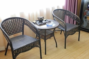 Una habitación con dos sillas de mimbre y una mesa redonda pequeña, una tetera y una bandeja con una taza y platillo.