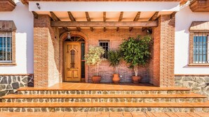 A building with a wooden door, brick walls, and a stone foundation. There are steps leading to the entrance, and potted plants are placed on the right side. - Villa Sol Nerja - Five Bedroom Villa, Sleeps 9 (Nerja)