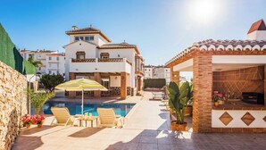 A pool area with lounge chairs and a table, surrounded by potted plants and a stone wall. - Villa Sol Nerja - Five Bedroom Villa, Sleeps 9 (Nerja)