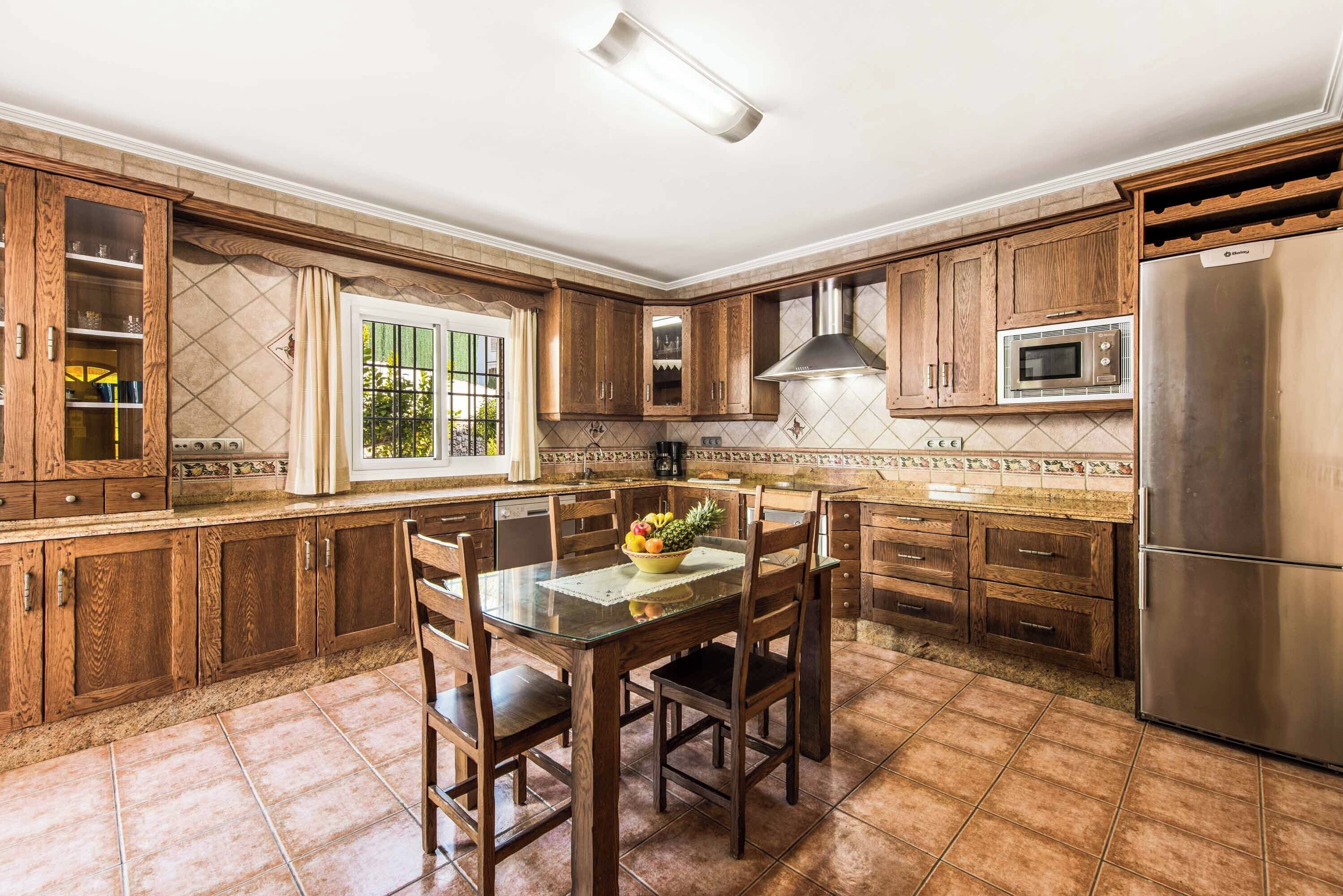 A kitchen with wooden cabinets, a stainless steel refrigerator, and a dining table with chairs.