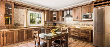 A kitchen with wooden cabinets, a stainless steel refrigerator, and a dining table with chairs.