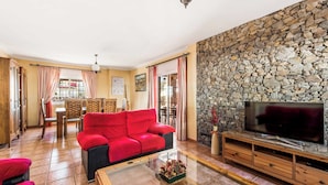 A living room with a red sofa, a glass coffee table, a stone wall, and a TV. - Villa Sol Nerja - Five Bedroom Villa, Sleeps 9 (Nerja)