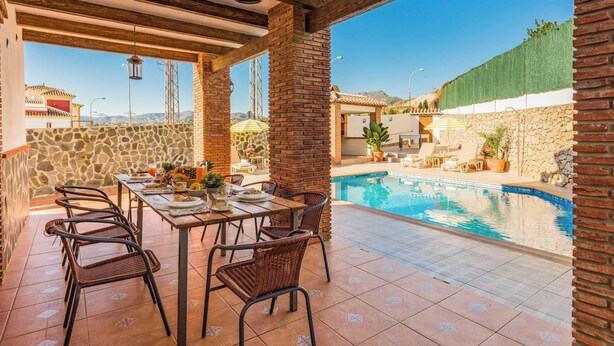 An outdoor patio with a pool, stone walls, and a dining area with wicker chairs and a table set for two. - Villa Sol Nerja - Five Bedroom Villa, Sleeps 9 (Nerja)