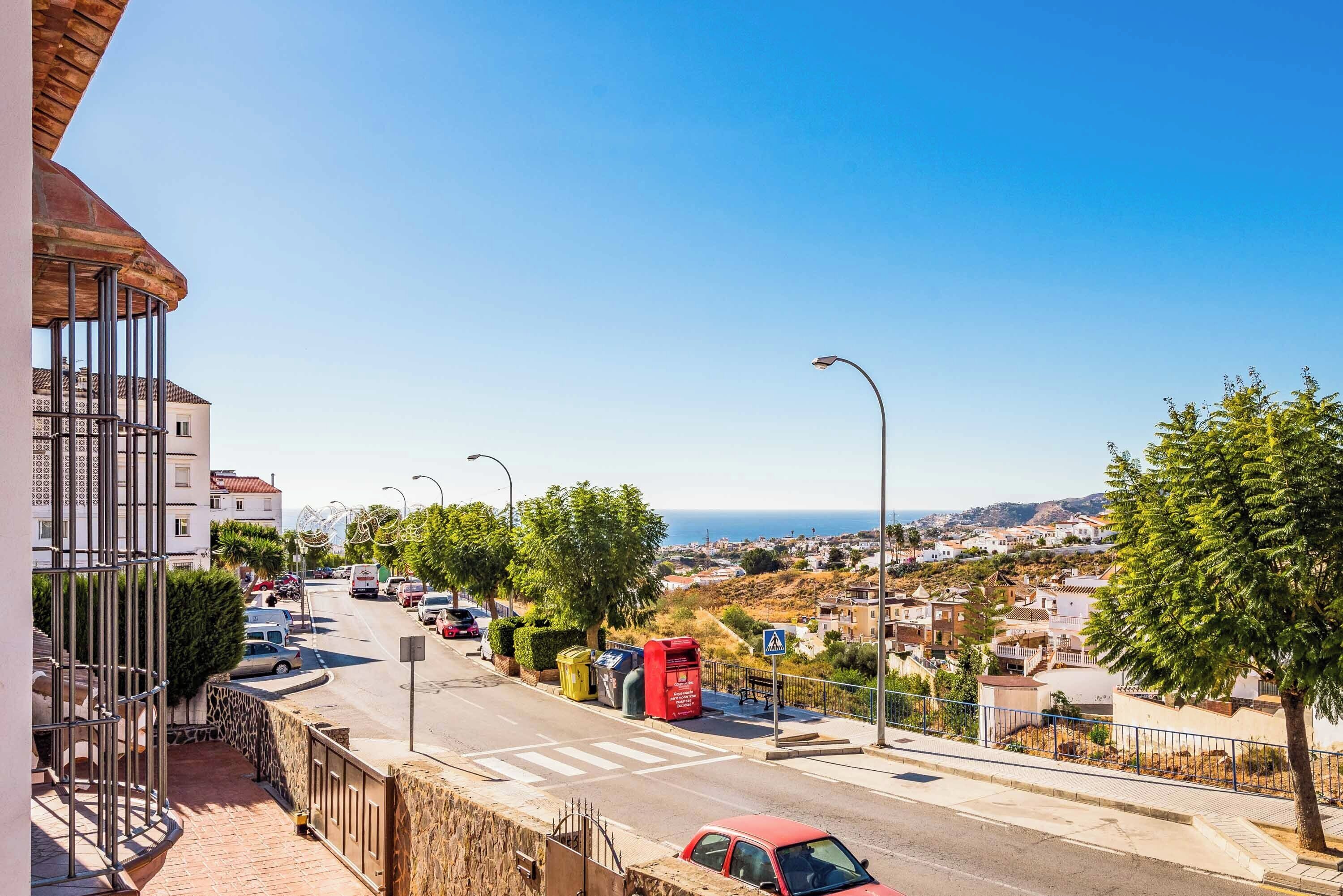 A street view with a clear sky, a red car, and a pedestrian crossing.