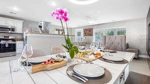 A modern kitchen with white cabinets, a microwave, and a dining area set for a meal with a centerpiece of pink orchids. - Luxury Heated Salt Pool House in Perfect Location (Tampa)