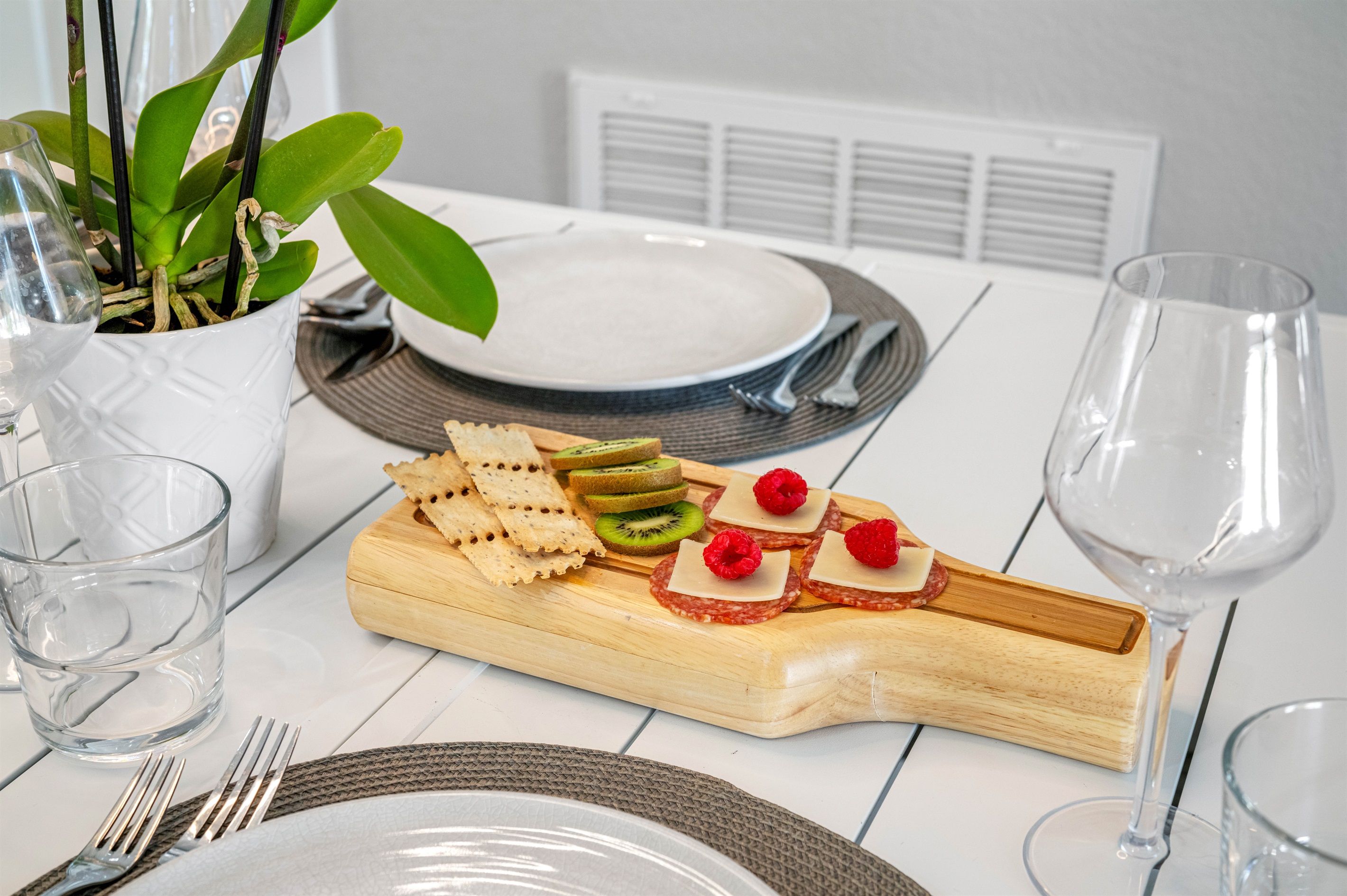 A dining table set with plates, cutlery, glasses, and a wooden board with snacks.