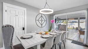 A dining area with a white table set for four, a modern pendant light, and a view of the outdoor patio. - Luxury Heated Salt Pool House in Perfect Location (Tampa)