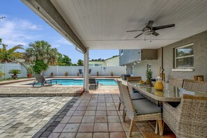 A covered outdoor area with a pool, wicker furniture, and a ceiling fan.