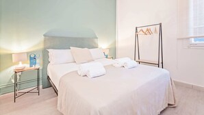 Ein ordentlich bezogenes Bett mit weißen Leinentüchern und Handtüchern, ein Nachttisch mit einer Lampe und ein Kleiderständer an der Wand.