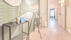 Ein Flur mit einer modernen Lampe, einem kleinen Tisch mit einer Vase und einer Karte, und Blick in einen weiteren Raum.
