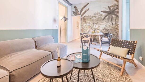 Ein modernes Wohnzimmer mit einer Couch, zwei runden Tischen, einer Bank und einer Wandmalerei von tropischem Grünwerk.