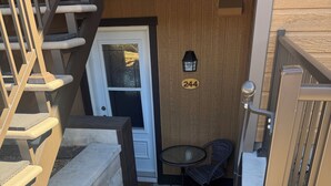 A staircase leading to a door with the number 244, a small outdoor seating area with a table and chairs, and a wooden wall.