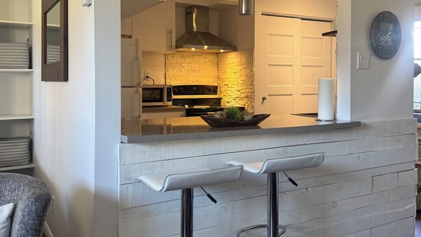 A modern kitchen with a stone backsplash, stainless steel appliances, and a bar area with stools.
