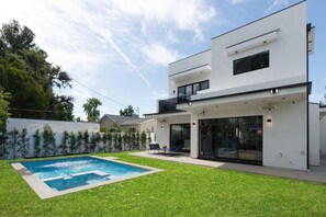 Uma casa moderna de dois andares com piscina, um alpendre coberto e gramado bem cuidado.