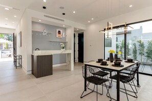Een moderne keuken met een centraal eiland, een eethoek met een tafel en stoelen, en grote ramen met uitzicht op de omgeving.