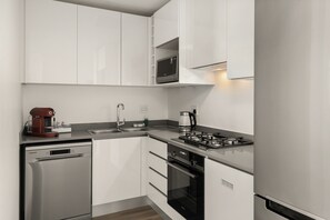 A modern kitchen with white cabinets, a built-in microwave, a coffee maker, a sink, and a stove.