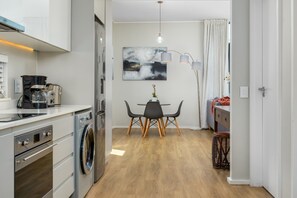 A compact kitchen with modern appliances, a dining area with a table and chairs, and a large window with curtains.