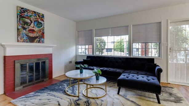 A living room with a fireplace, a black sofa, a round coffee table, and a colorful painting above the fireplace.