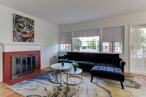 Un salon avec une cheminée, un canapé noir, une table basse ronde et un tableau coloré accroché au-dessus de la cheminée.