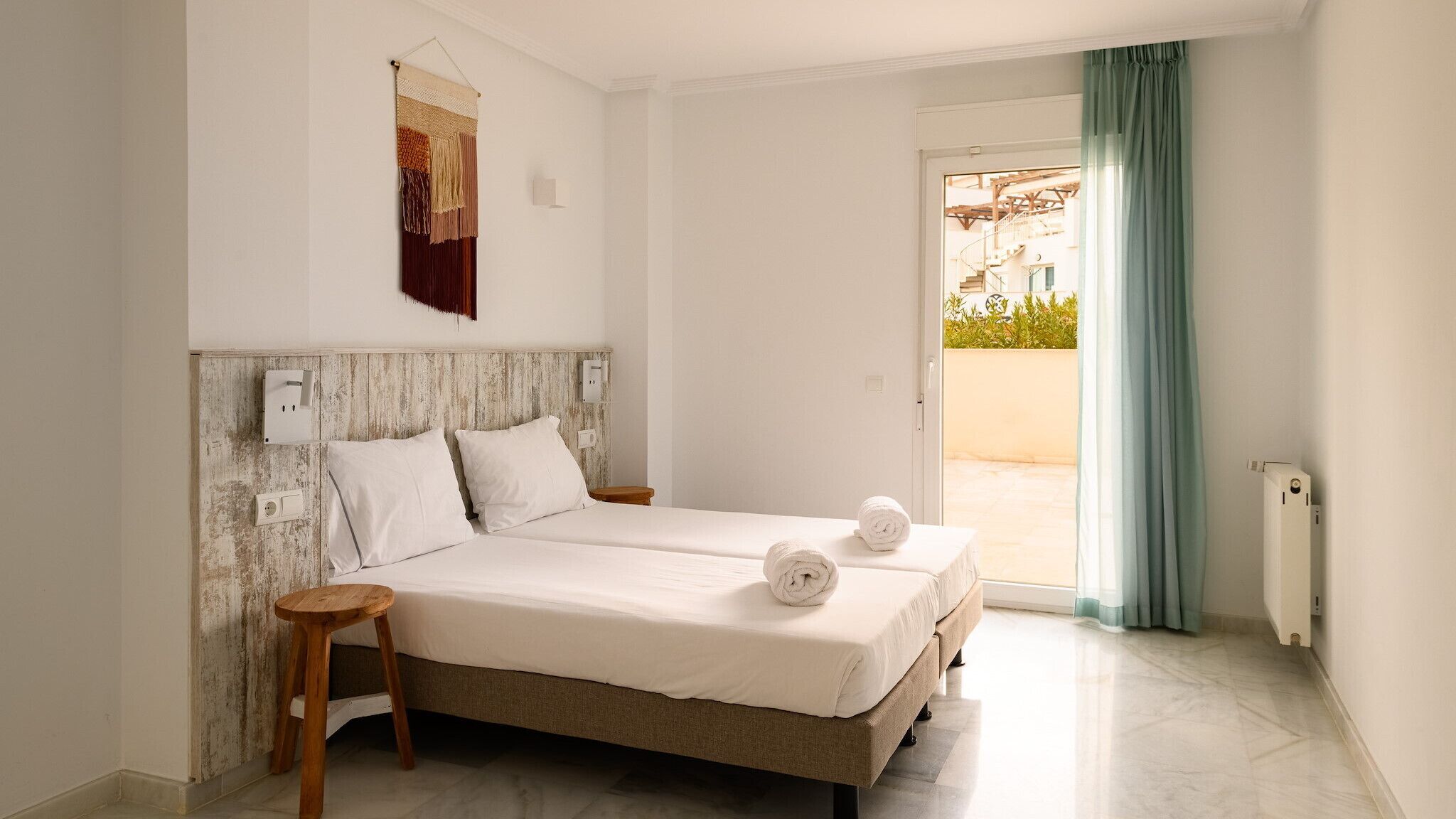 Una cama doble con sábanas blancas, un cabecero de madera y un taburete pequeño de madera.