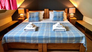 Une chambre avec un plafond en pente, une couvre-lit à carreaux, deux oreillers, deux tables de chevet avec des lampes et deux serviettes pliées posées sur le lit.
