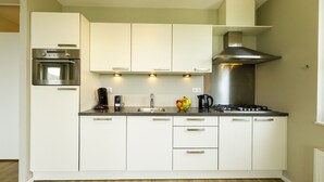 A modern kitchen with white cabinets, a built-in oven, a gas stove, and a coffee maker.