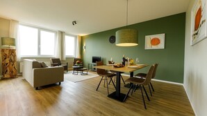 A modern living room with a dining area, wooden flooring, and green walls.