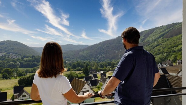 Two people overlooking a scenic landscape with mountains and houses.