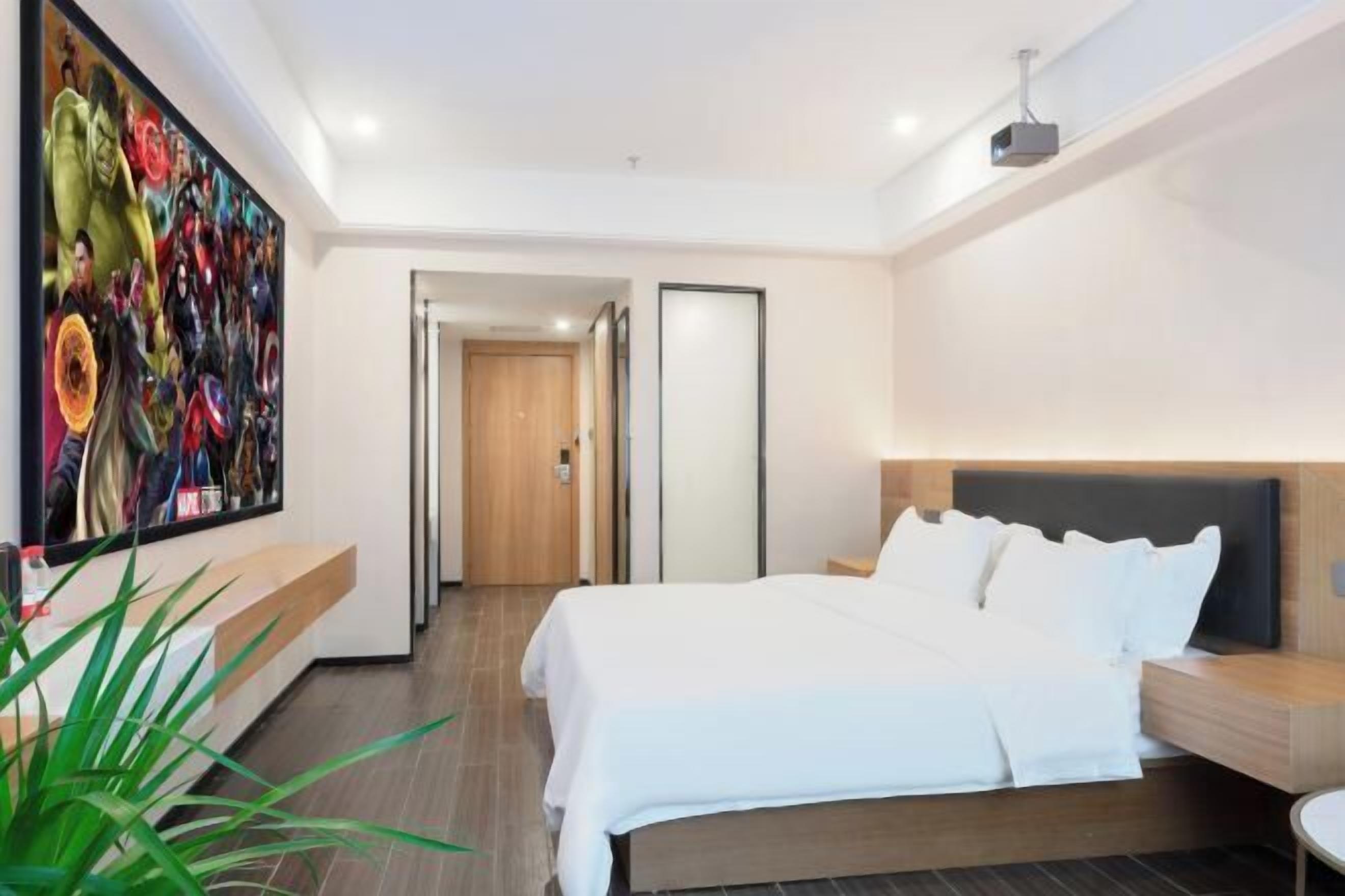 Quarto de hotel moderno com uma cama grande, uma mesa de cabeceira, uma luminária e uma grande obra de arte na parede, além de uma porta que dá para outro cômodo.