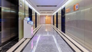 A modern hotel corridor with glass walls, a digital information kiosk, and a polished marble floor.