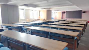 A classroom with rows of desks, a projector screen, and windows.