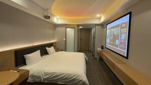 A modern hotel room with a bed, a bedside table, a TV screen, and a ceiling projector.