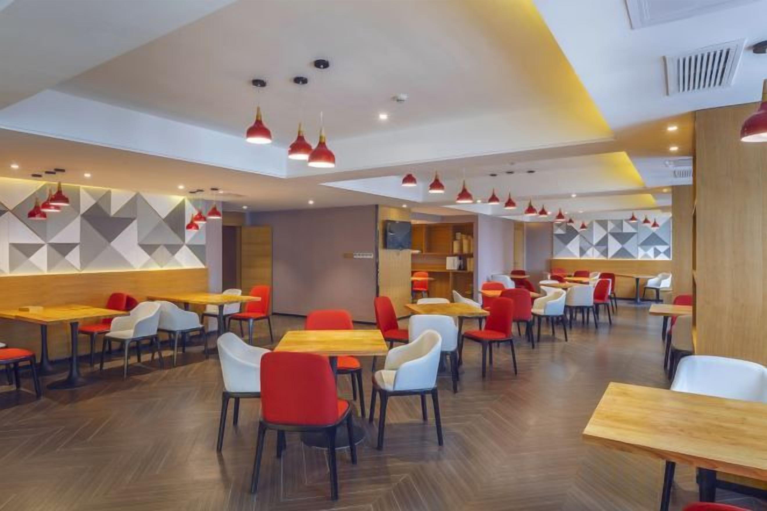 Un restaurante moderno con varias mesas y sillas, un diseño geométrico en la pared e iluminación colgante.