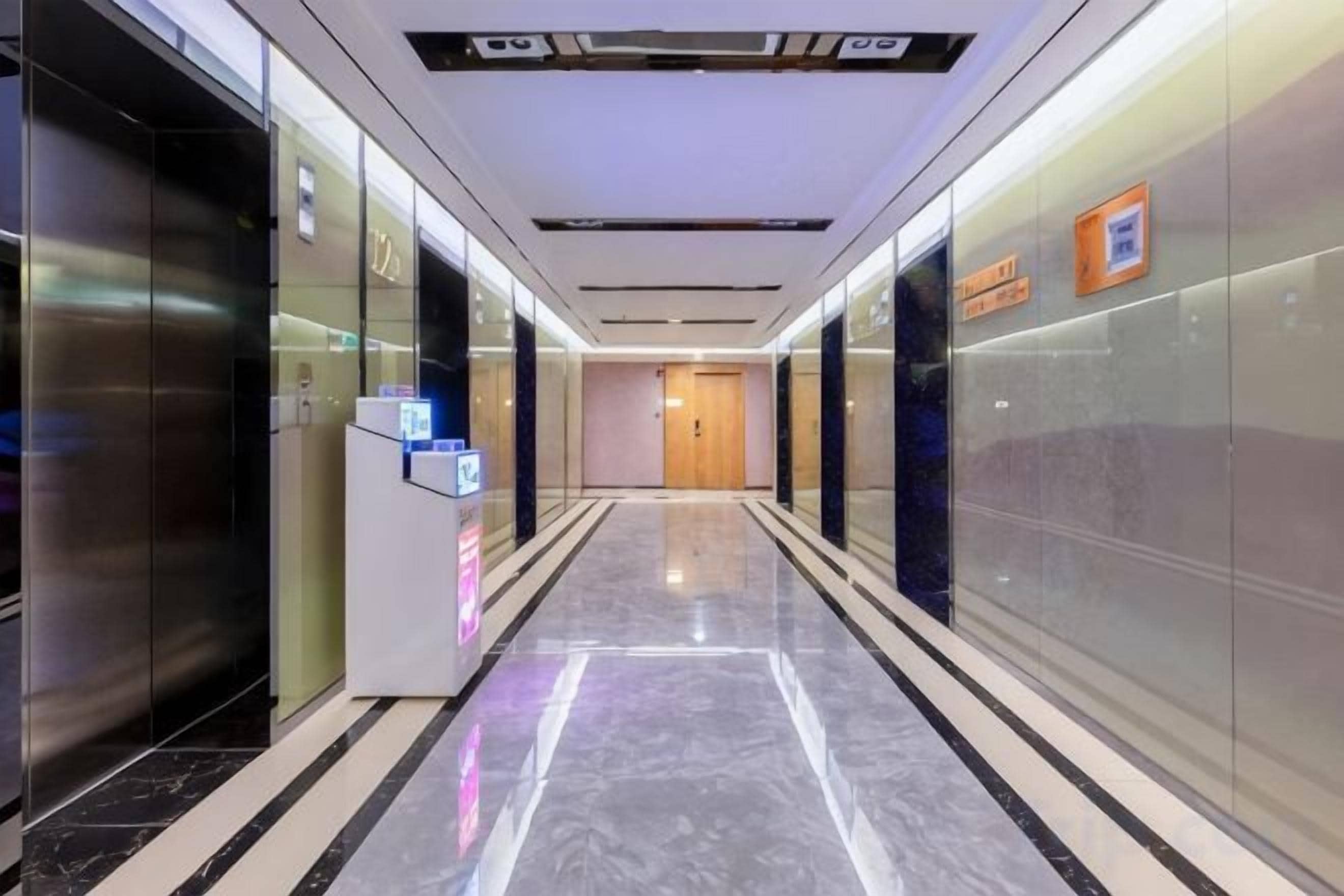 A hotel corridor with glass doors, a reception desk, and a wooden door at the end.