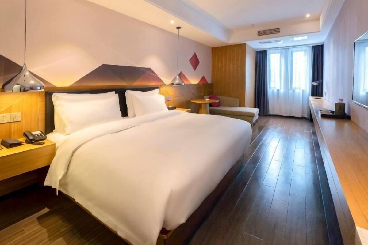 A hotel room with a large bed, bedside tables, a desk, a chair, and a window with curtains.